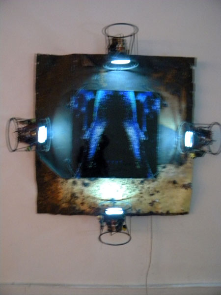 Œuvre frontale de Maxence Denis, alliant photographie, téléviseurs, vitre de verre et tôle métallique Œuvre frontale de Maxence Denis, alliant photographie, téléviseurs, vitre de verre et tôle métallique